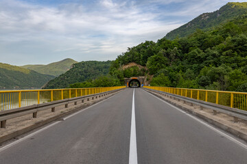  A straight asphalt road with yellow guardrails on both sides leads towards a tunnel entrance,...