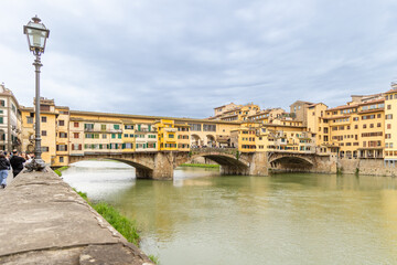 Obraz premium Florence, Italy - April 10, 2024: View of the Vecchio Bridge in Florence with tourists crowding its surroundings in Florence, Italy
