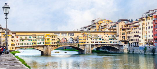 Fototapeta premium Florence, Italy - April 10, 2024: View of the Vecchio Bridge in Florence with tourists crowding its surroundings in Florence, Italy