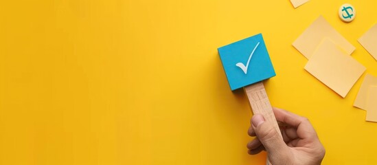 A hand holds a wooden block with a blue check mark stamp