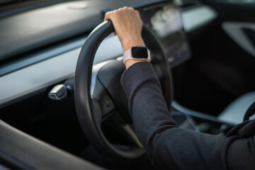 Woman hand on the steering wheel of a car. Smartwatch on businesswoman hand. Cropped. Lifestyle, driving, transport concept