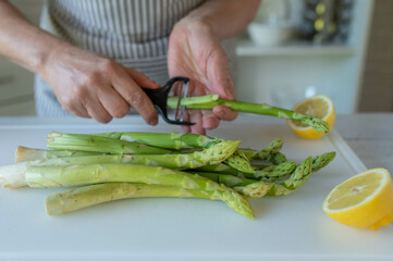 Peeling green asparagus in the kitchen on a cutting board by woman´s hands