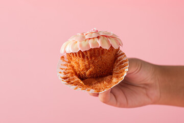 Female hand showing a cupcake in foreground. Pink background.