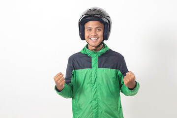 Portrait of Asian online taxi driver wearing green jacket and helmet raising his fist, celebrating success. Isolated image on white background