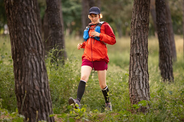 A woman is running through a forest wearing a red jacket and black hat. She is wearing black socks...