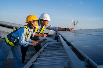 Two people are standing on a roof, one pointing at something. They are wearing safety gear and...