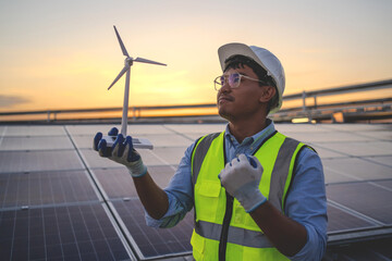 A man in a yellow vest holding a wind turbine. The man is wearing a hard hat and safety glasses