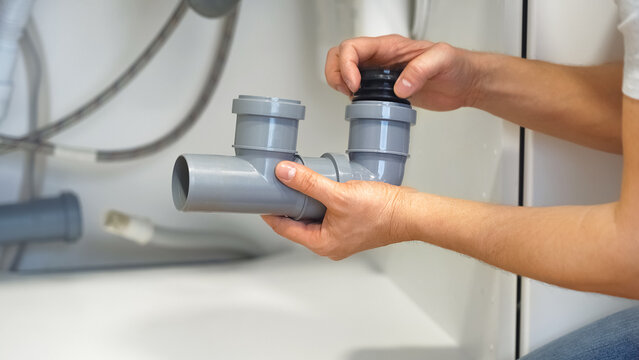 Close up of hands of plumber repairs plumbing pipes sewerage in kitchen sink. Plumbing replacement gasket. Replacement of plumbing pipes.