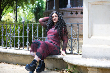 Latin woman, brunette with curly hair, young and beautiful and overweight sitting on a bench in a...
