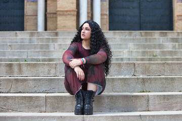 Latin woman, brunette with curly hair, young and beautiful sitting on the stairs in a city park....