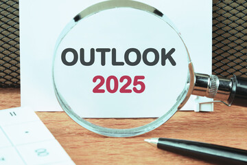 Business and financial trends. OUTLOOK 2025 text through a magnifying glass on a white sheet