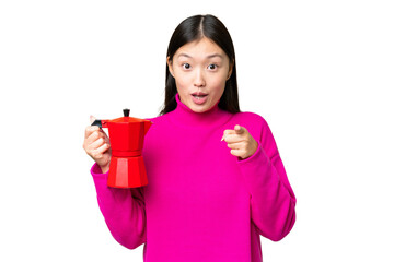 Young Asian woman holding coffee pot over isolated chroma key background surprised and pointing front