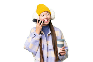 Young Asian woman wearing winter muffs over isolated chroma key background holding coffee to take away and a mobile