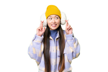 Young Asian woman wearing winter muffs over isolated chroma key background with fingers crossing