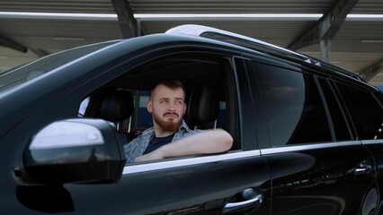 Young man sitting in the car, holding hand on steering wheel. Slow motion