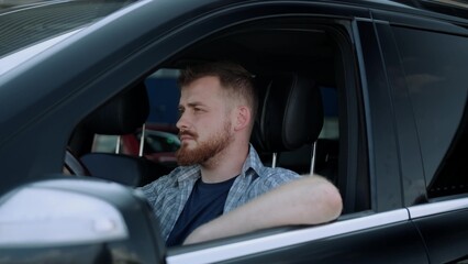 Bearded young man holding hand on the steering wheel in the car. Slow motion
