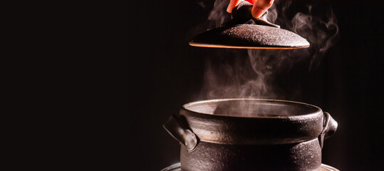 A boiling clay pot steams up as a chef opens the lid of a cooking steam pot in a restaurant.