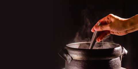 A boiling clay pot steams up as a restaurant's chef uses a ladle to stir soup in a cooking pot 