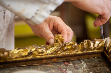 Artigianato, artigiano. Restauro di cornice dorata d'antiquariato, mani in primo piano al lavoro.