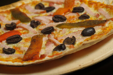 Pizza with ham, tomato and olives on a black background