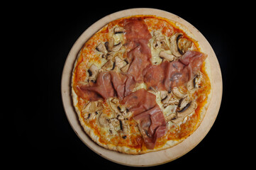 Pizza with ham, mushrooms and cheese on a wooden plate.