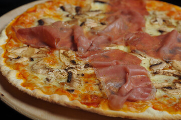 Pizza with ham, mushrooms and cheese on a wooden plate.