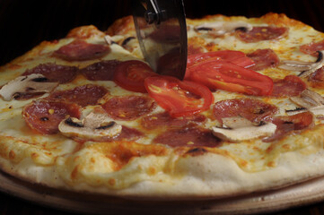 process of cutting pizza with ham, cheese and tomatoes on a wooden board.