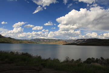 a wide lake on a grassy mountain side under a blue sky