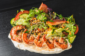 Colorful shrimp salad with mixed greens, tomatoes, cucumbers, and nuts on a dark surface