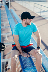 Man sitting on a blue bench, wearing a cap