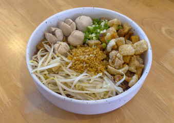 Classic Thai Tossed Noodles in the white bowl. Thai-styled noodles with pork belly popcorn, meatballs and bean sprout is served on the table. 