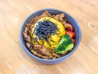 Teriyaki pork rice bowl with omelet and vegetable served on the table. Grilled pork and omelet in Japanese-style donburi.