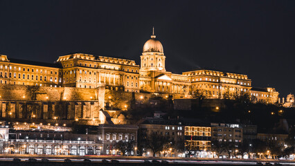 Obraz premium the view of a castle lit up at night as seen from across a river