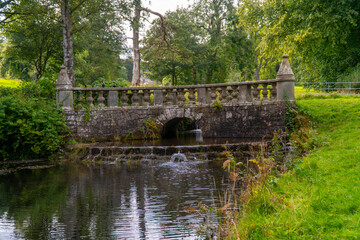 the stone bridge has two small fountains running under it and the grass is beside