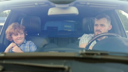 Smiling father driving car while his little son sitting next to him. Slow motion