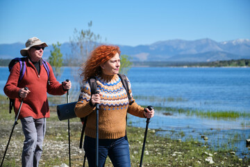 A mature couple of hikers are walking by the border of a lake.