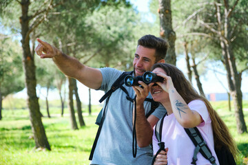 A man and a woman are looking through binoculars in a park. The man is pointing to something in the distance