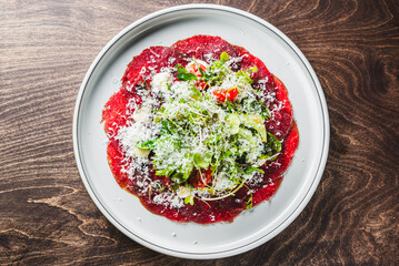 A vibrant plate of beef carpaccio garnished with fresh greens, cheese shavings, and cherry tomatoes on a white plate