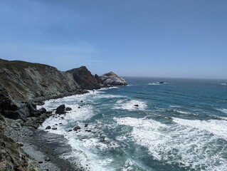 Foamy waves of an ocean hitting the rocks on the shore with the horizon in the sunny background