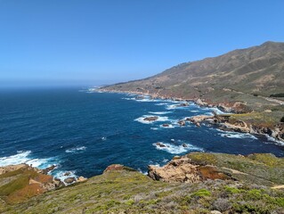 Foamy waves of an ocean hitting the rocks on the shore with the horizon in the sunny background