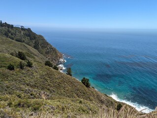 Foamy waves of an ocean hitting the rocks on the shore with the horizon in the sunny background
