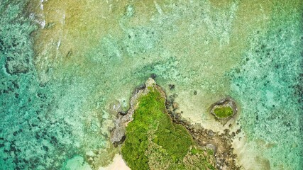 Aerial view of a tranquil turquoise bay with a mossy rock formation