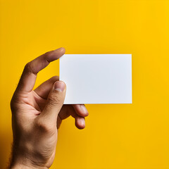 Hand holding a blank business card on yellow background.