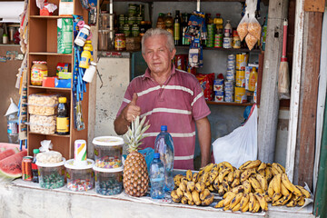 Stall, vendor and man with thumbs up for selling fruit with success, nutrition and agreement for health goals. Food, like emoji and entrepreneur with banana and thank you for outdoor market in Brazil