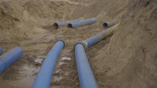 Thick gray water pipes lie in ditch for repair replacement. Construction site for sewerage with large diameter pipes in clay pit