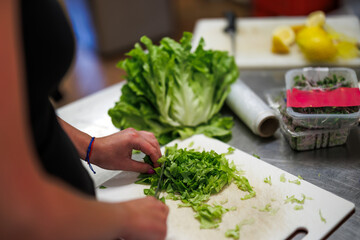 Woman chopping lettuce salad by knife on cutting board in kitchen. Preparing food for healthy eating