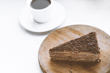 Piece of chocolate cake on a wooden plate with a cup of coffee