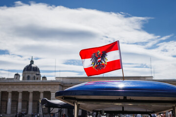 Austrian flag with coat of arms on a tourist vehicle at the Heldenplatz at Hofburg in Vienna. National flag of Austria against the sky