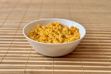 Yellow rice porridge cooked in milk with pumpkin spice in a white bowl on bamboo background. Close-up