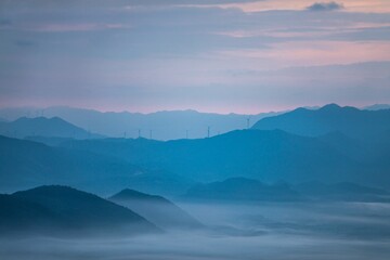 Drone shot of silhouettes of green-covered hills in mist at sunset, cool for background